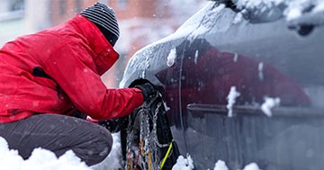 man putting snow chains on car tires
