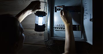 man checking breaker box with flashlight during power outage